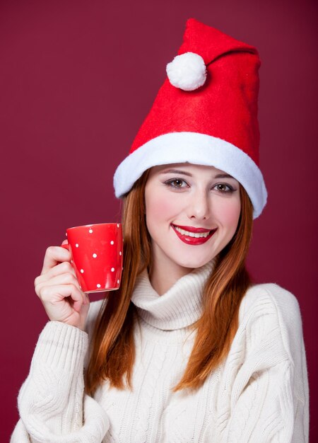 Garota ruiva com chapéu de natal com copo