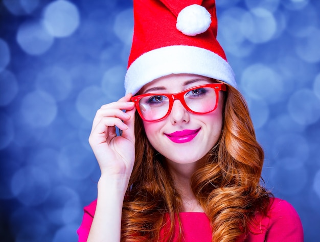 Garota ruiva com chapéu de Natal e óculos com presente cinza