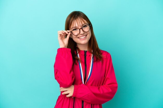 Garota ruiva com medalhas isoladas de fundo azul com óculos e feliz