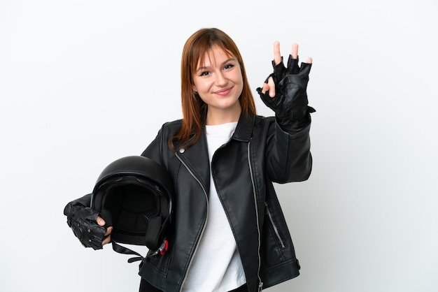 Garota ruiva com um capacete de moto isolado no fundo branco feliz e contando três com os dedos