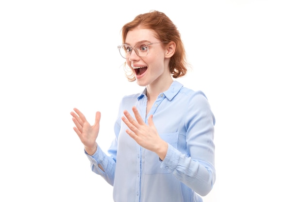Garota ruiva de rosto chocado na camisa de negócios parece surpresa com a boca aberta espalha as mãos no fundo branco do estúdio