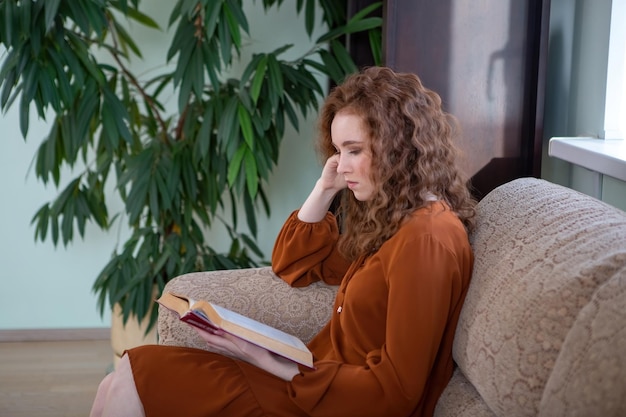 Garota ruiva em casa lendo um livro em um sofá aconchegante