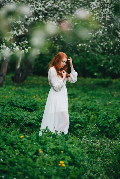 Garota ruiva linda em um vestido branco entre macieiras florescendo no jardim