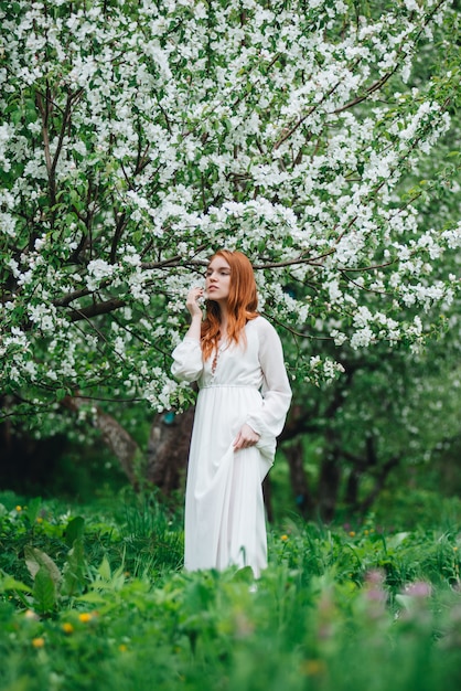 Garota ruiva linda em um vestido branco entre macieiras florescendo no jardim