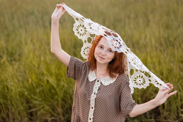 Garota ruiva posando em um prado de verão ao pôr do sol com um vestido elegante