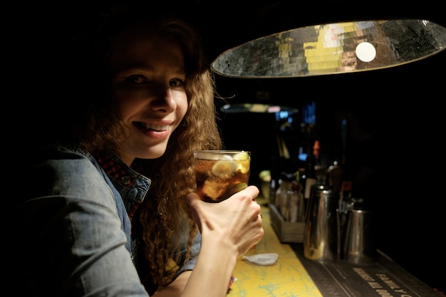 Garota ruiva sentada no bar (pub) bebendo coquetel gelado e sorrindo