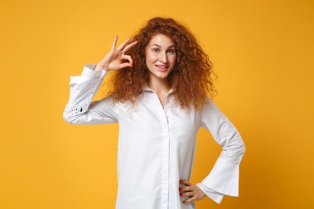 Garota ruiva sorridente em uma camisa branca casual posando isolada em uma parede laranja amarela