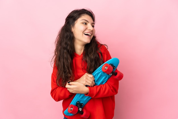 Garota russa adolescente isolada em um fundo rosa com um skate e uma expressão feliz