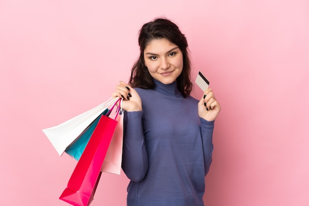 Garota russa adolescente isolada em um fundo rosa segurando sacolas de compras e um cartão de crédito