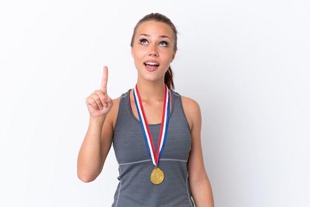 Garota russa jovem esportiva com medalhas isoladas em fundo branco apontando para cima e surpresa