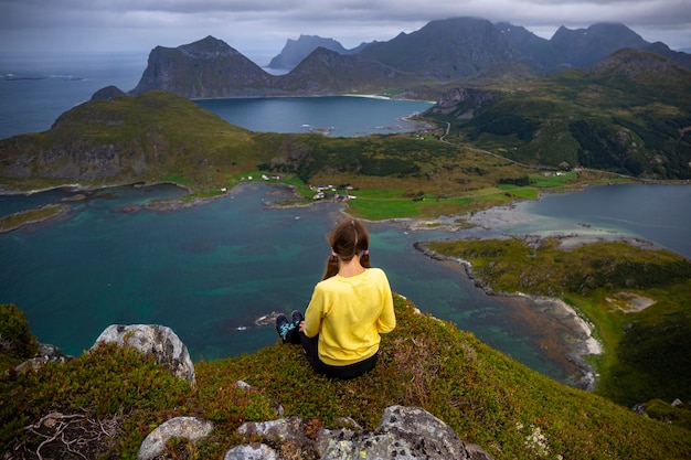 Garota se senta em cima de Offersoykammen apreciando o panorama das ilhas lofoten, Noruega caminhando