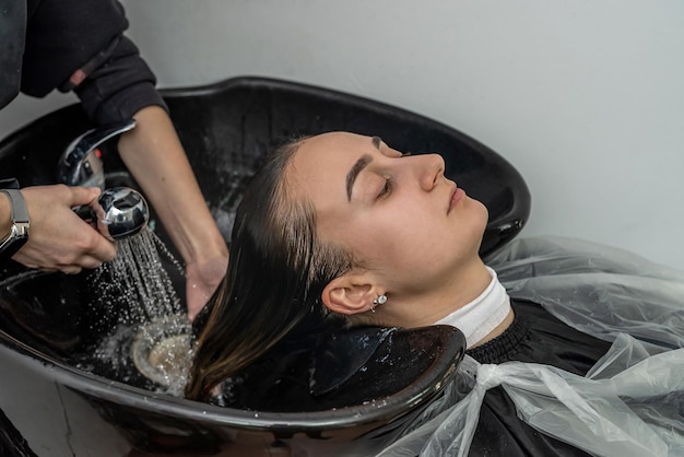 Garota se senta em um salão onde seu mestre colorista lava a cabeça e o cabelo para aplicar tinta