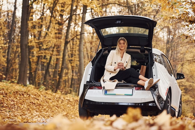 Garota se senta na parte de trás do carro. Automóvel novo moderno na floresta.