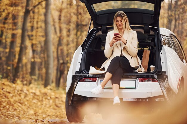 Garota se senta na parte de trás do carro. Automóvel novo moderno na floresta.