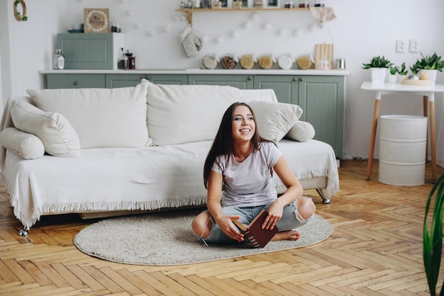 Garota se senta no chão com livro nas mãos morena no interior aconchegante da casa Blogging em casa