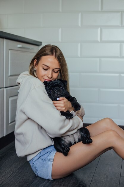 Garota segurando um cachorro pug preto nos braços em casa