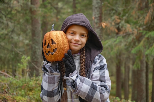 Garota segurando uma lanterna de abóbora decorativa brilhante garota do conceito de halloween na floresta brincando com lanterna de jack