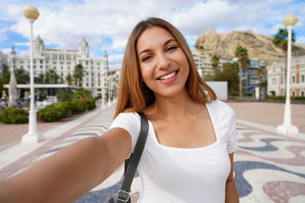 Foto garota selfie em alicante, espanha. auto-retrato de jovem com a casa carbonell e o monte benacantil com o castelo de santa bárbara ao fundo.