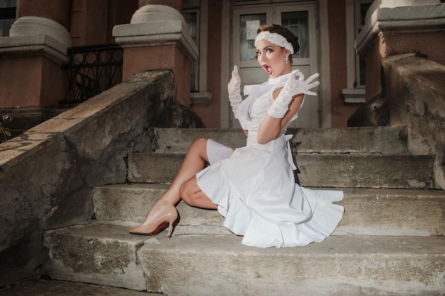 Garota sentada nas escadas do velho pisca sorrisos gestosMenina em roupas brancas estilo dos anos 80