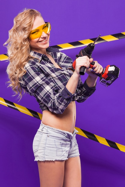Garota sexy construtor jovem na camisa chechered, óculos e shorts brancos estão com serra electro