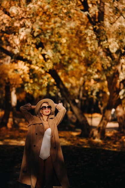 Garota sexy em um casaco e chapéu em um parque ensolarado de outono