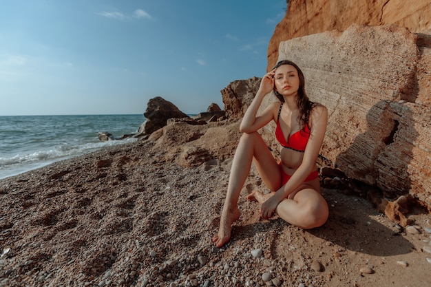 Garota sexy em um maiô vermelho está sentada na praia