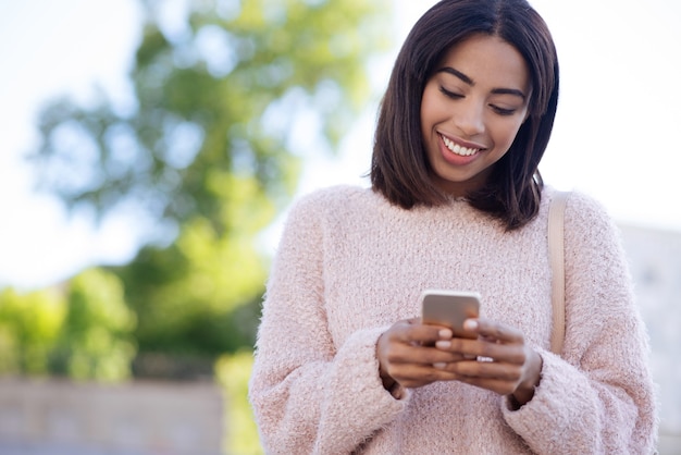 Garota simpática e enérgica confiante usando seu smartphone para se comunicar com seus amigos e respondê-los em segundos
