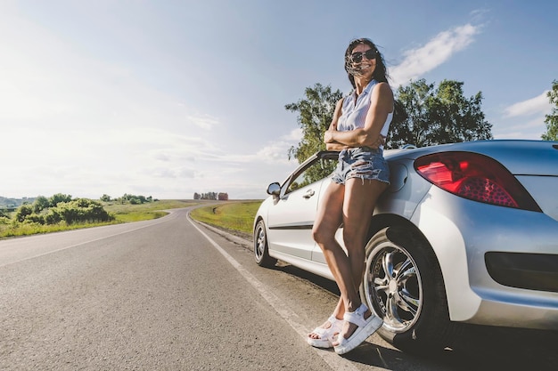 Garota sob o sol brilhante na estrada com carro cabriolet O conceito de aventura e viajar sozinho Viagens rodoviárias pedindo carona Garota de fim de semana de verão fica em seu carro quebrado e esperando por ajuda