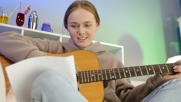 Garota sonhadora tocando violão em casa. Músico feminino aprendendo a tocar instrumento musical na sala de estar.