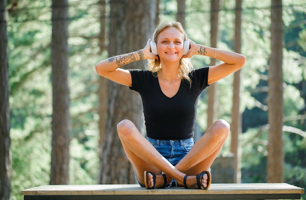 Garota sorridente com fone de ouvido está posando para a câmera sentada no fundo da natureza