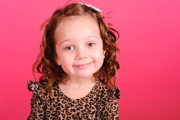 Garota sorridente de 4 a 5 anos usa vestido estampado de leopardo se divertindo sobre fundo rosa no estúdio