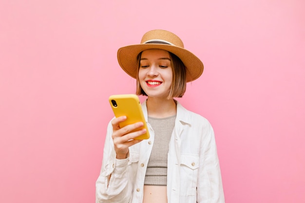 Garota sorridente de chapéu e roupas leves usa a internet em um smartphone com um sorriso no rosto