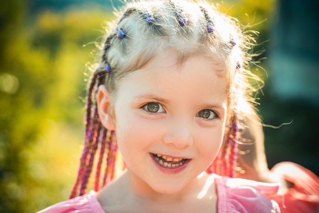 Garota sorridente de criança com dreadlocks de penteado garoto com cabelo da moda em fundo desfocado ao ar livre