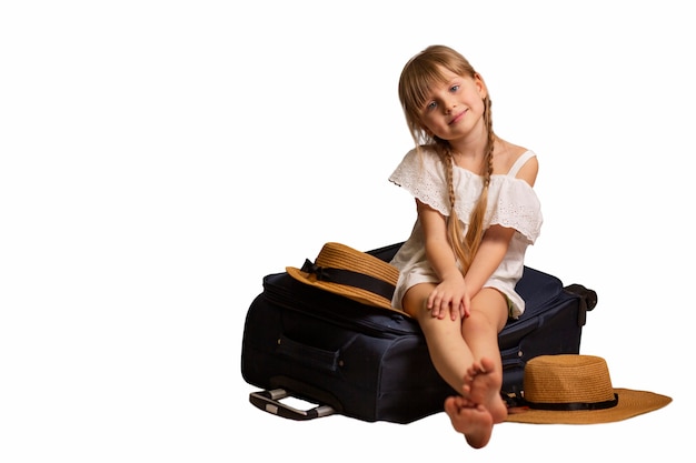 Garota sorridente e feliz sentada em uma mala de bagagem, mala de viagem em um quarto de hotel