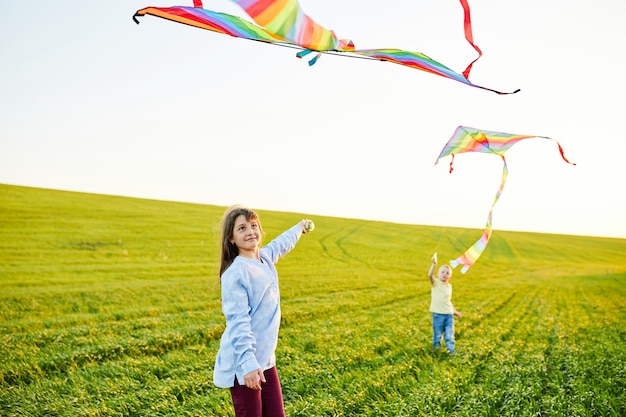 Garota sorridente e irmão correndo com pipas coloridas voando no prado de grama alta Momentos felizes da infância