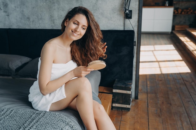 Garota sorridente escova cabelos longos e saudáveis com escova de cabelo após o banho no quarto Anúncio de cosméticos Haircare