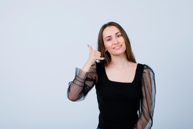 Garota sorridente está mostrando gesto de telefone segurando a mão perto da orelha no fundo branco