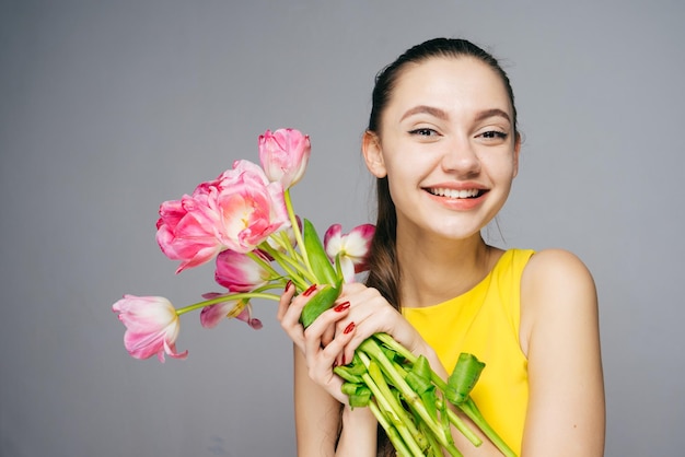 Garota sorridente feliz de vestido amarelo está segurando nas mãos flores rosa perfumadas sorrindo