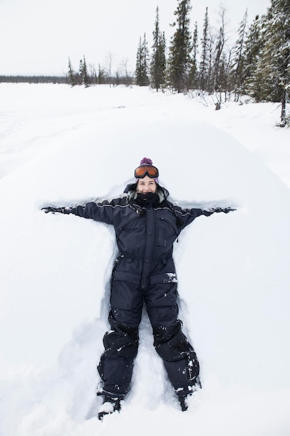 Garota sorridente feliz deitada na neve fazendo figura de anjo