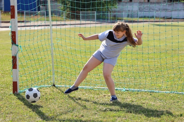 Garota sorridente gordinha em roupas esportivas fica no portão de futebol e quer parar a bola