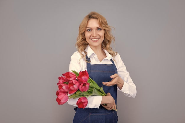 Garota sorridente no avental com flores de tulipa da primavera em fundo cinza