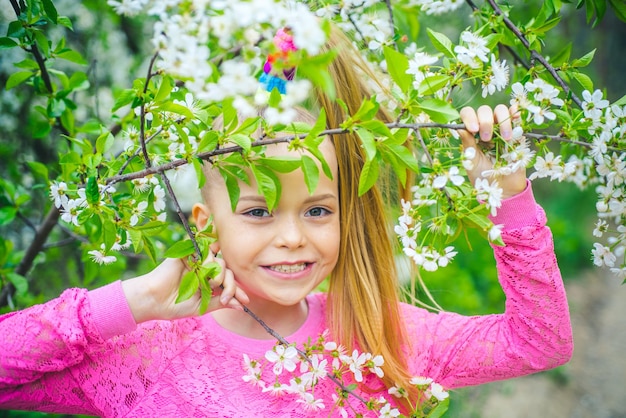 Garota sorridente parada ao ar livre atrás dos galhos de uma árvore Conceito de primavera Andar em um ato de parque