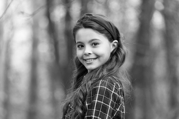 Garota sorridente usa faixa de cabeça com nó Maiores tendências de acessórios de cabelo Adorável menina vestida de camisa xadrez vermelha faixa de cabeça vermelha Acessórios de tendência de moda Fundo de natureza infantil extravagante Faixa de cabeça acolchoada