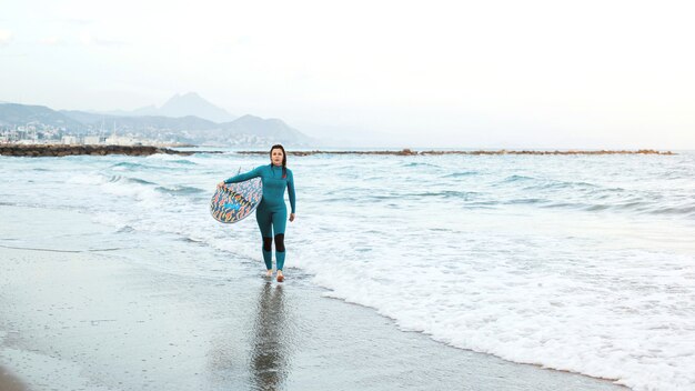 Garota surfista andando com prancha na praia. Mulher de surfista. Mulher jovem e bonita na praia. Esportes Aquáticos. Estilo de vida ativo e saudável. Férias de verão. Esporte radical.