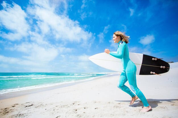 Garota surfista correndo na praia com sua prancha de surf