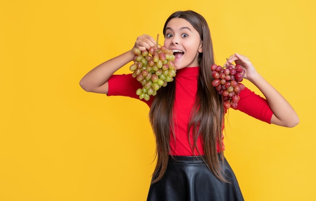 Garota surpresa segura cacho de uvas em fundo amarelo