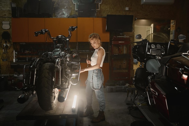 Garota talentosa vestindo macacão azul usando ferramenta de trabalho para consertar motocicleta