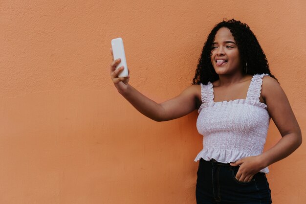 Garota tomando uma selfie engraçada na frente da parede laranja.