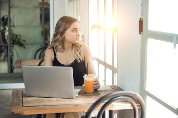 Garota trabalhadora de Freeland Sentada em um café em uma mesa de madeira tomando café e usando o smartphone na mesa como laptop Jovem mulher navegando na internet conversando blogando