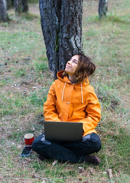 Garota trabalhando com seu computador sentado na floresta